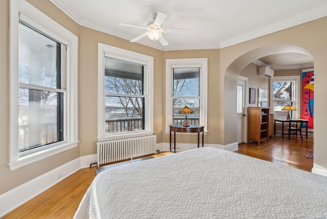 bedroom featuring radiator, hardwood / wood-style flooring, ornamental molding, ceiling fan, and a wall mounted AC