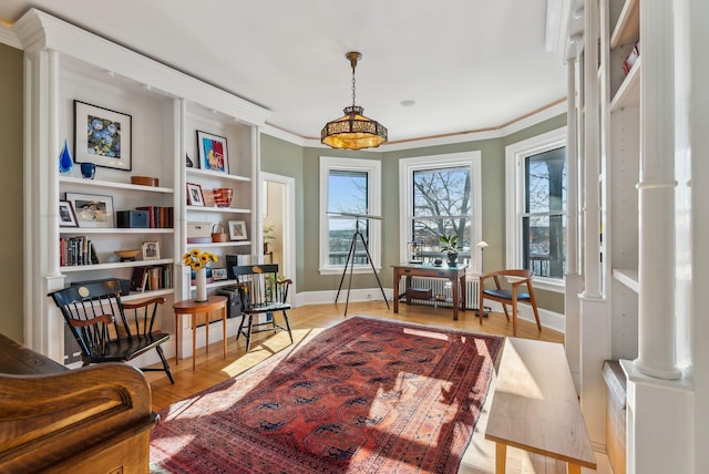 sitting room with crown molding, radiator, ornate columns, and light wood-type flooring