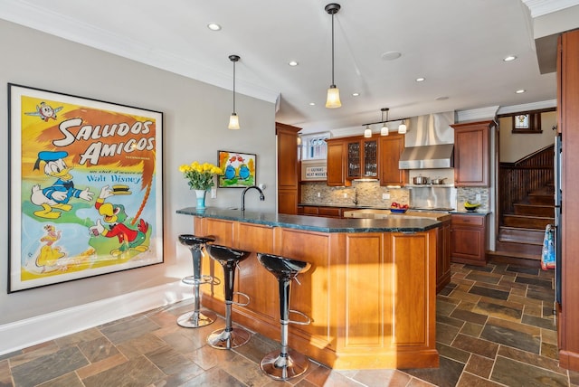 kitchen featuring crown molding, hanging light fixtures, backsplash, wall chimney range hood, and a breakfast bar area