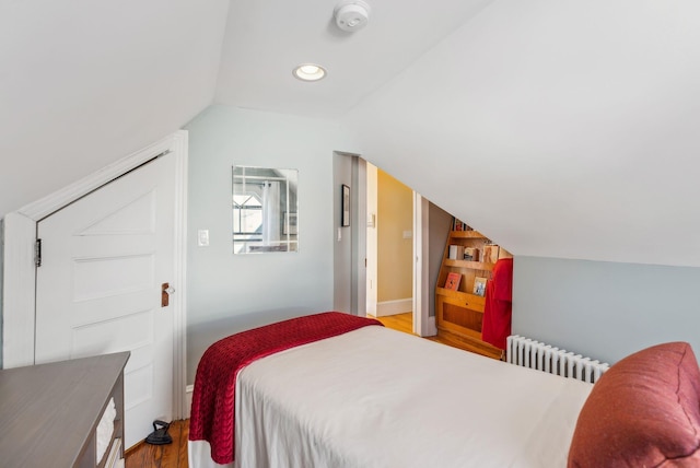 bedroom featuring light hardwood / wood-style floors, radiator, and vaulted ceiling