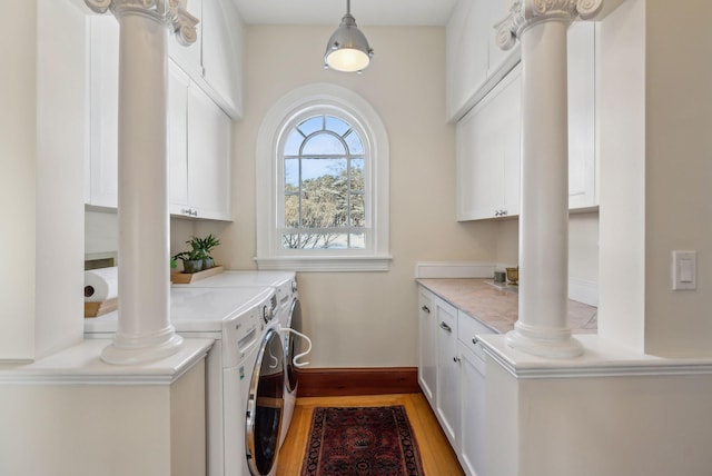 laundry area with decorative columns, cabinets, light hardwood / wood-style flooring, and independent washer and dryer