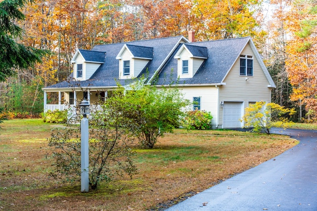 new england style home featuring a porch, a front lawn, and a garage