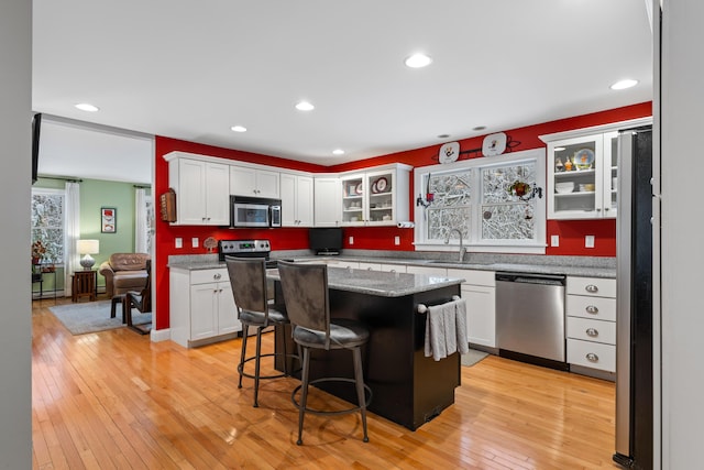 kitchen featuring a center island, stainless steel appliances, light wood-type flooring, white cabinets, and a kitchen breakfast bar