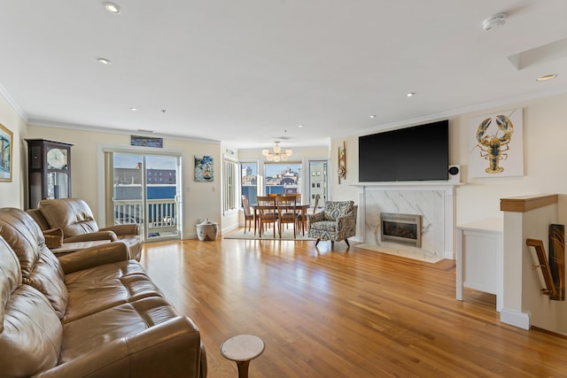 living room featuring a high end fireplace, light wood-type flooring, a chandelier, and ornamental molding