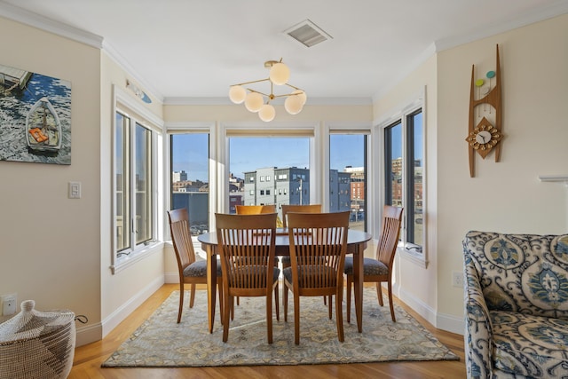 dining area with ornamental molding, light wood-type flooring, and a notable chandelier