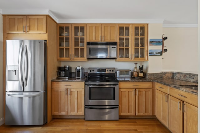 kitchen featuring light hardwood / wood-style floors, dark stone countertops, ornamental molding, and stainless steel appliances