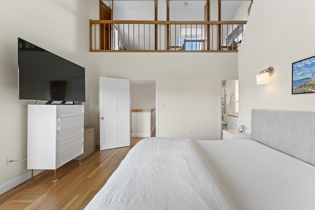 bedroom featuring ensuite bathroom, wood-type flooring, and a high ceiling