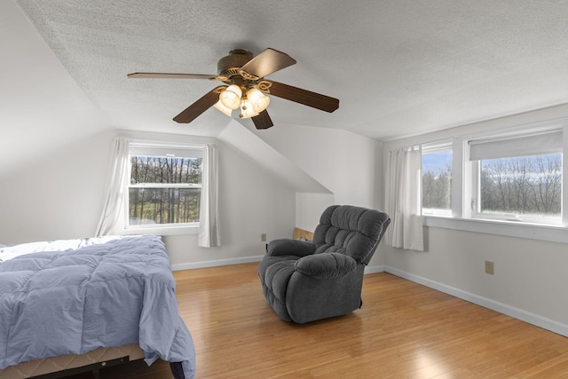 bedroom featuring a textured ceiling, light hardwood / wood-style flooring, vaulted ceiling, and ceiling fan