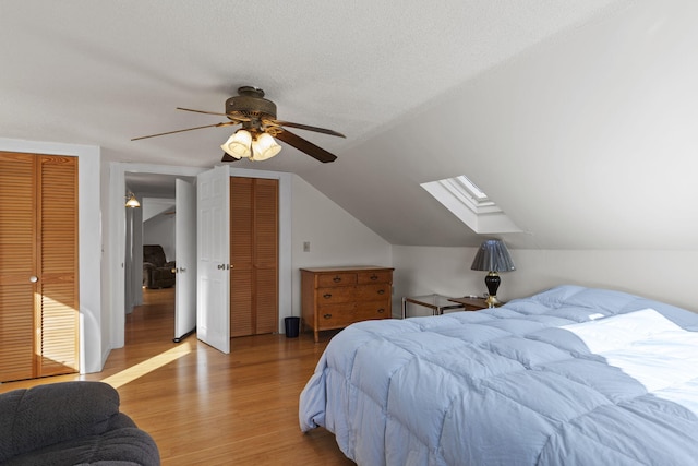 bedroom with lofted ceiling with skylight, light hardwood / wood-style flooring, ceiling fan, a textured ceiling, and multiple closets