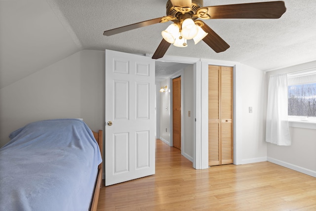 bedroom with ceiling fan, light hardwood / wood-style floors, a textured ceiling, vaulted ceiling, and a closet