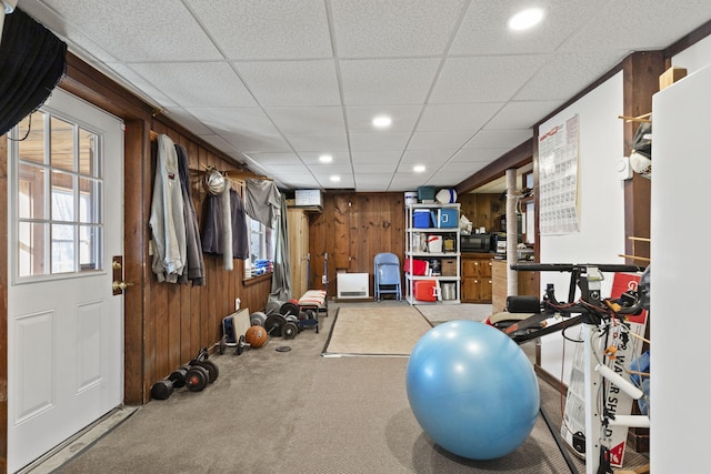 workout room featuring carpet flooring, wooden walls, and a drop ceiling