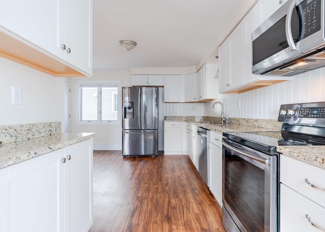 kitchen with white cabinets, sink, dark hardwood / wood-style floors, light stone countertops, and appliances with stainless steel finishes