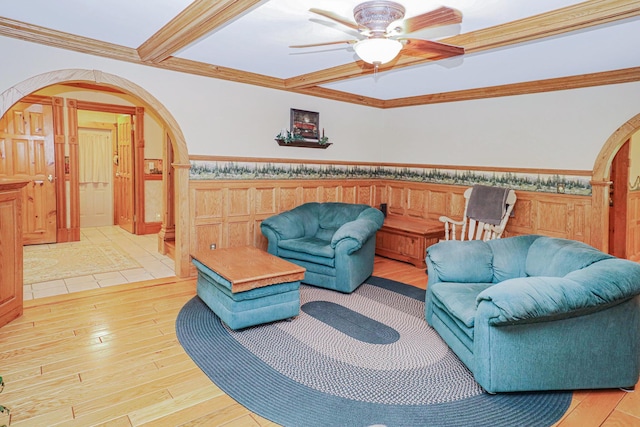 living room with arched walkways, light wood-type flooring, wainscoting, and crown molding