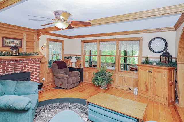 living room with a wainscoted wall, a ceiling fan, a brick fireplace, wood-type flooring, and crown molding