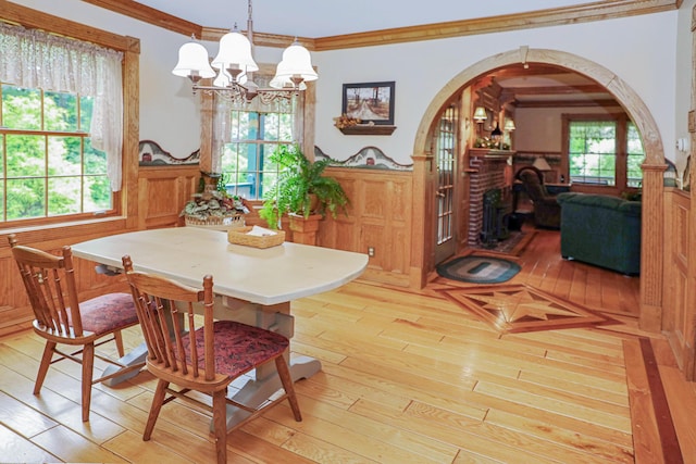 dining space featuring arched walkways, a wainscoted wall, crown molding, light wood finished floors, and a brick fireplace