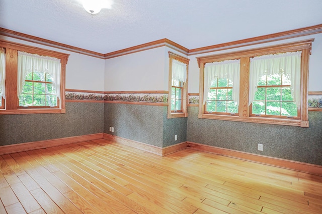 spare room featuring a wainscoted wall, hardwood / wood-style floors, crown molding, and wallpapered walls