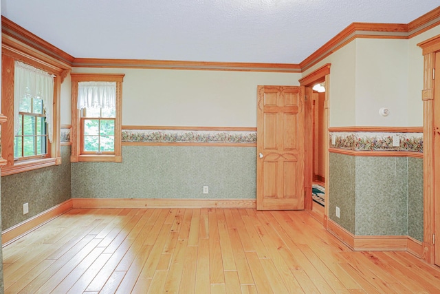 empty room featuring wallpapered walls, crown molding, baseboards, and hardwood / wood-style floors