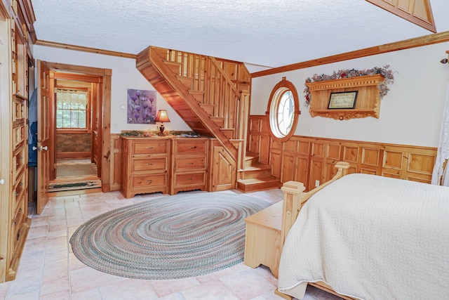 bedroom featuring a textured ceiling, ornamental molding, and wainscoting