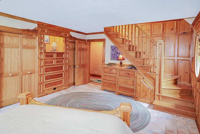 bedroom with wood walls, stone finish floor, a textured ceiling, and ornamental molding