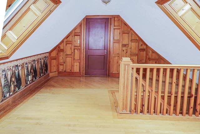 additional living space with vaulted ceiling with skylight, light wood finished floors, and wood walls