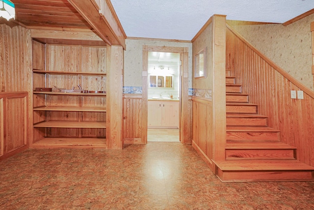 interior space with wooden walls, wainscoting, ornamental molding, and a textured ceiling