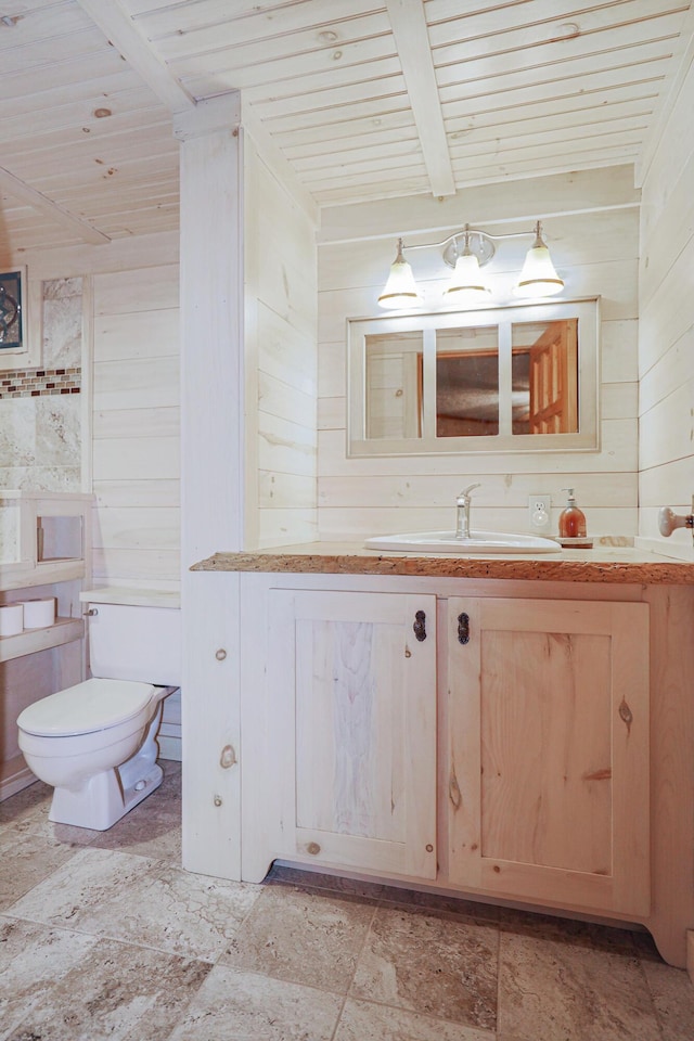 half bathroom featuring toilet, wood walls, vanity, wooden ceiling, and beamed ceiling