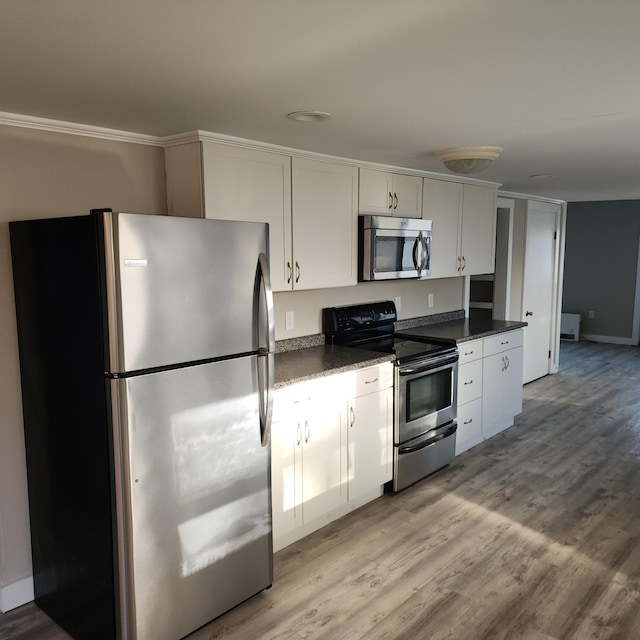 kitchen featuring dark stone countertops, white cabinets, light wood-type flooring, and appliances with stainless steel finishes