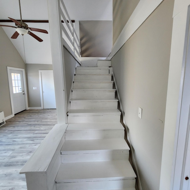 stairs with ceiling fan, vaulted ceiling, and hardwood / wood-style flooring