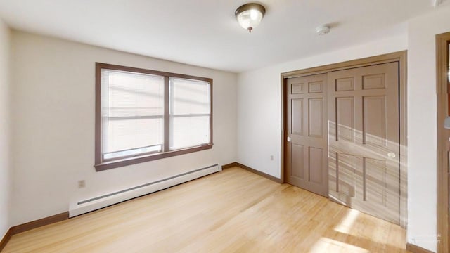 unfurnished bedroom featuring a closet, baseboard heating, and light hardwood / wood-style flooring