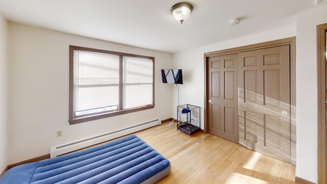 bedroom with hardwood / wood-style flooring, a baseboard radiator, and a closet