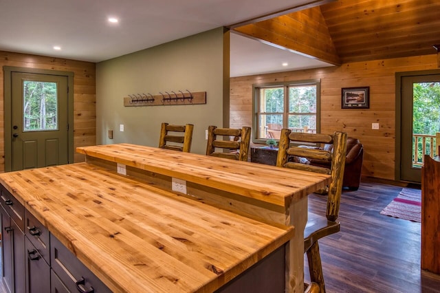 dining space with wood walls, dark wood-type flooring, and vaulted ceiling