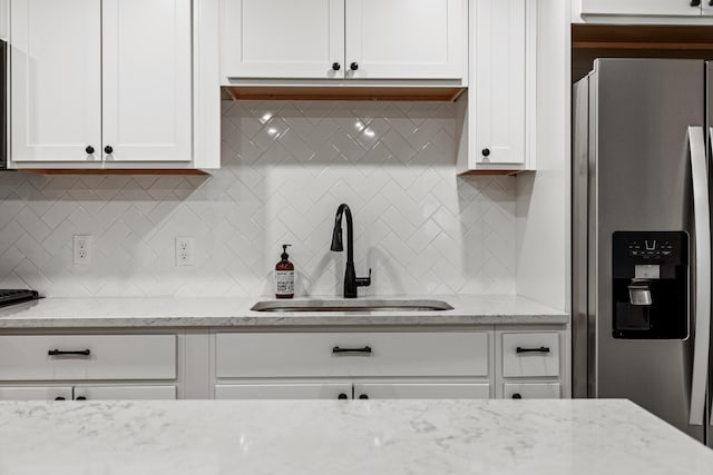 kitchen featuring sink, stainless steel fridge with ice dispenser, light stone countertops, tasteful backsplash, and white cabinetry