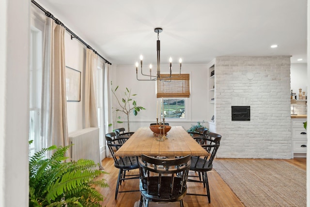 dining space with brick wall, a chandelier, radiator heating unit, and light wood-type flooring