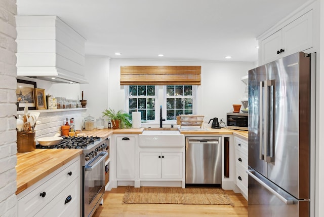 kitchen with wooden counters, premium appliances, sink, light hardwood / wood-style flooring, and white cabinets