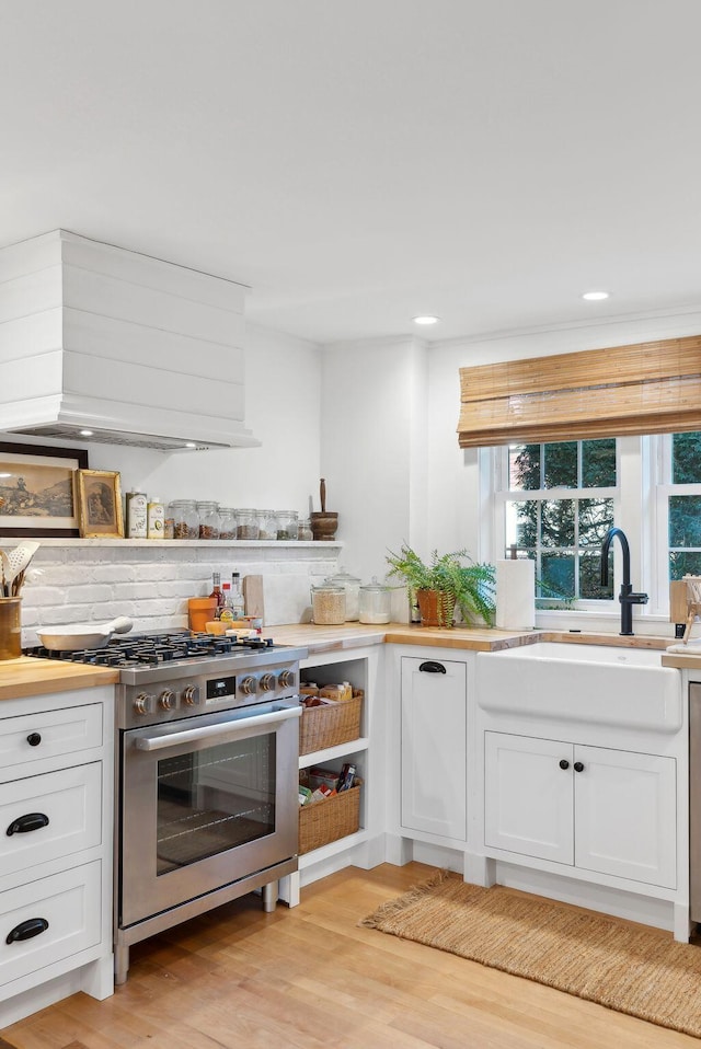 kitchen featuring sink, gas range, white cabinetry, light hardwood / wood-style flooring, and custom range hood