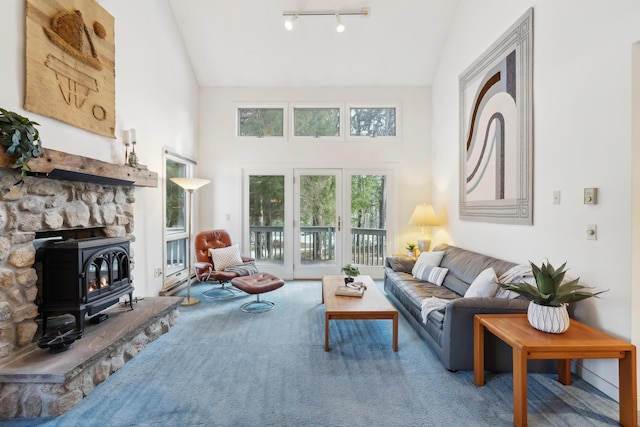 carpeted living room with a wood stove, high vaulted ceiling, and track lighting