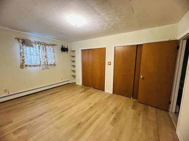 unfurnished bedroom with a baseboard heating unit, two closets, and light hardwood / wood-style floors