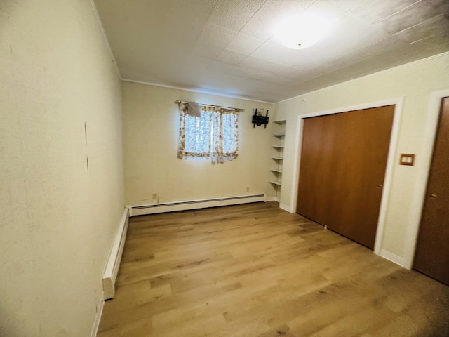 unfurnished bedroom with a closet, a baseboard heating unit, and hardwood / wood-style floors