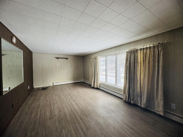 empty room featuring dark wood-type flooring, wooden walls, and a baseboard heating unit