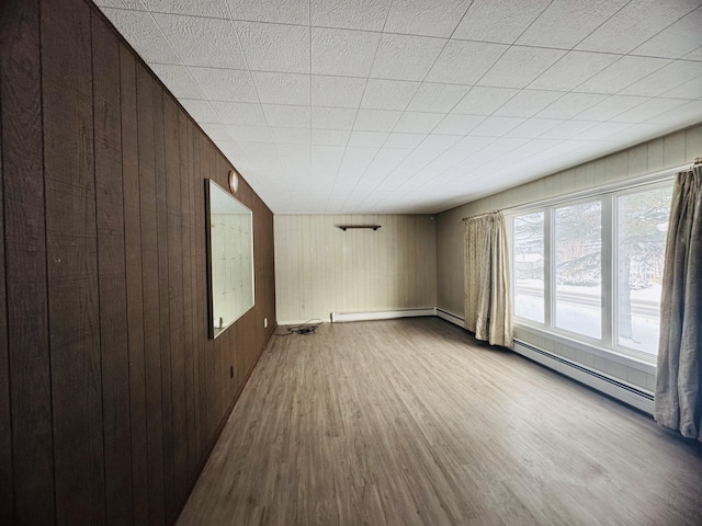 empty room with wood walls, baseboard heating, and light wood-type flooring