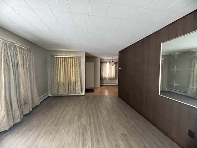 unfurnished room with baseboard heating, an inviting chandelier, wooden walls, and hardwood / wood-style flooring