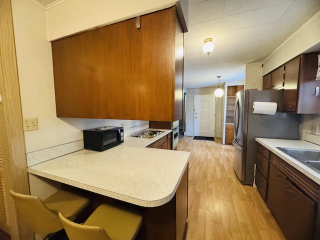 kitchen with kitchen peninsula, light hardwood / wood-style flooring, hanging light fixtures, appliances with stainless steel finishes, and sink