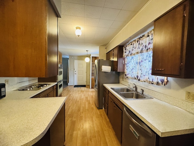 kitchen featuring sink, light wood-type flooring, kitchen peninsula, hanging light fixtures, and appliances with stainless steel finishes