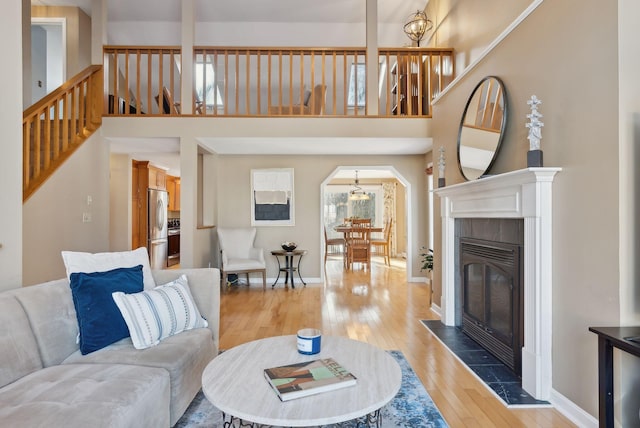 living room featuring a notable chandelier, a high ceiling, a tiled fireplace, and wood-type flooring