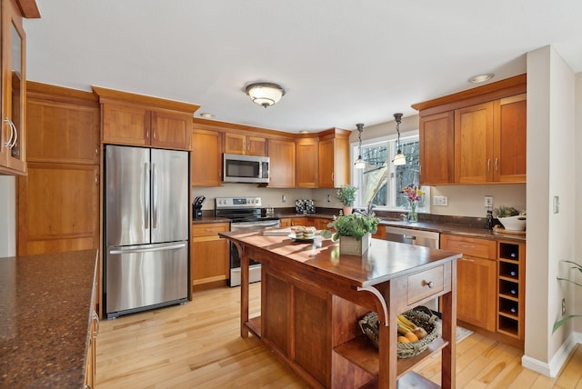 kitchen with decorative light fixtures, stainless steel appliances, light wood-type flooring, and dark stone countertops