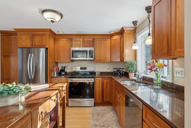 kitchen with sink, decorative light fixtures, dark stone countertops, light wood-type flooring, and appliances with stainless steel finishes