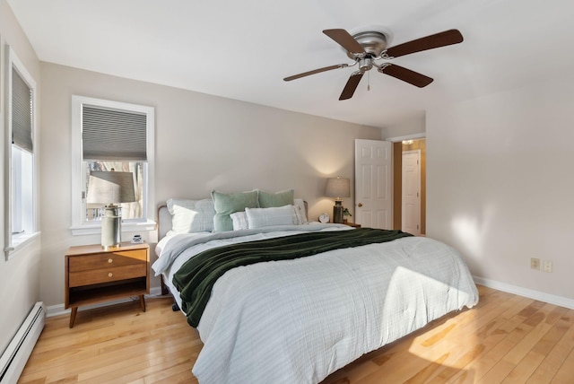 bedroom featuring ceiling fan, light hardwood / wood-style flooring, multiple windows, and a baseboard heating unit