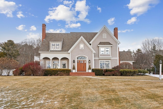 shingle-style home featuring a front lawn, a chimney, and a shingled roof