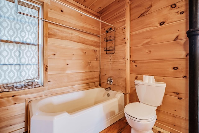 bathroom with wooden walls, washtub / shower combination, wood-type flooring, and toilet