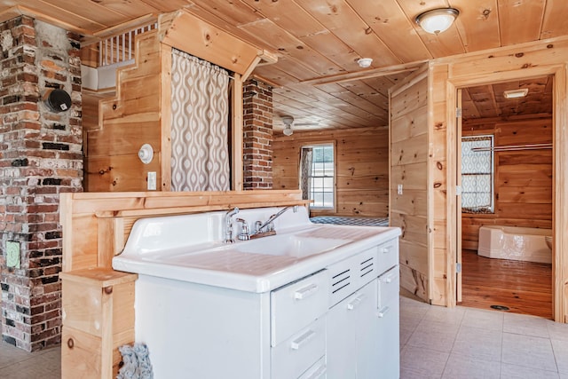 kitchen with white cabinets, wooden ceiling, wooden walls, and sink